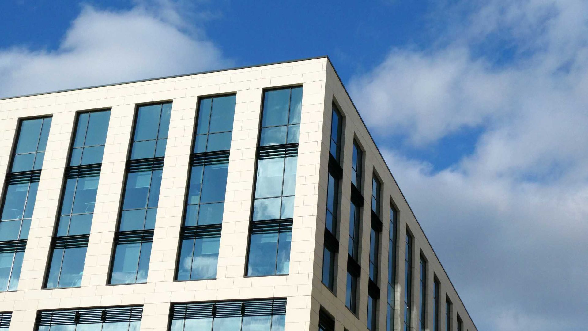 Modern white building with tall blue-tinted windows against a partly cloudy sky.