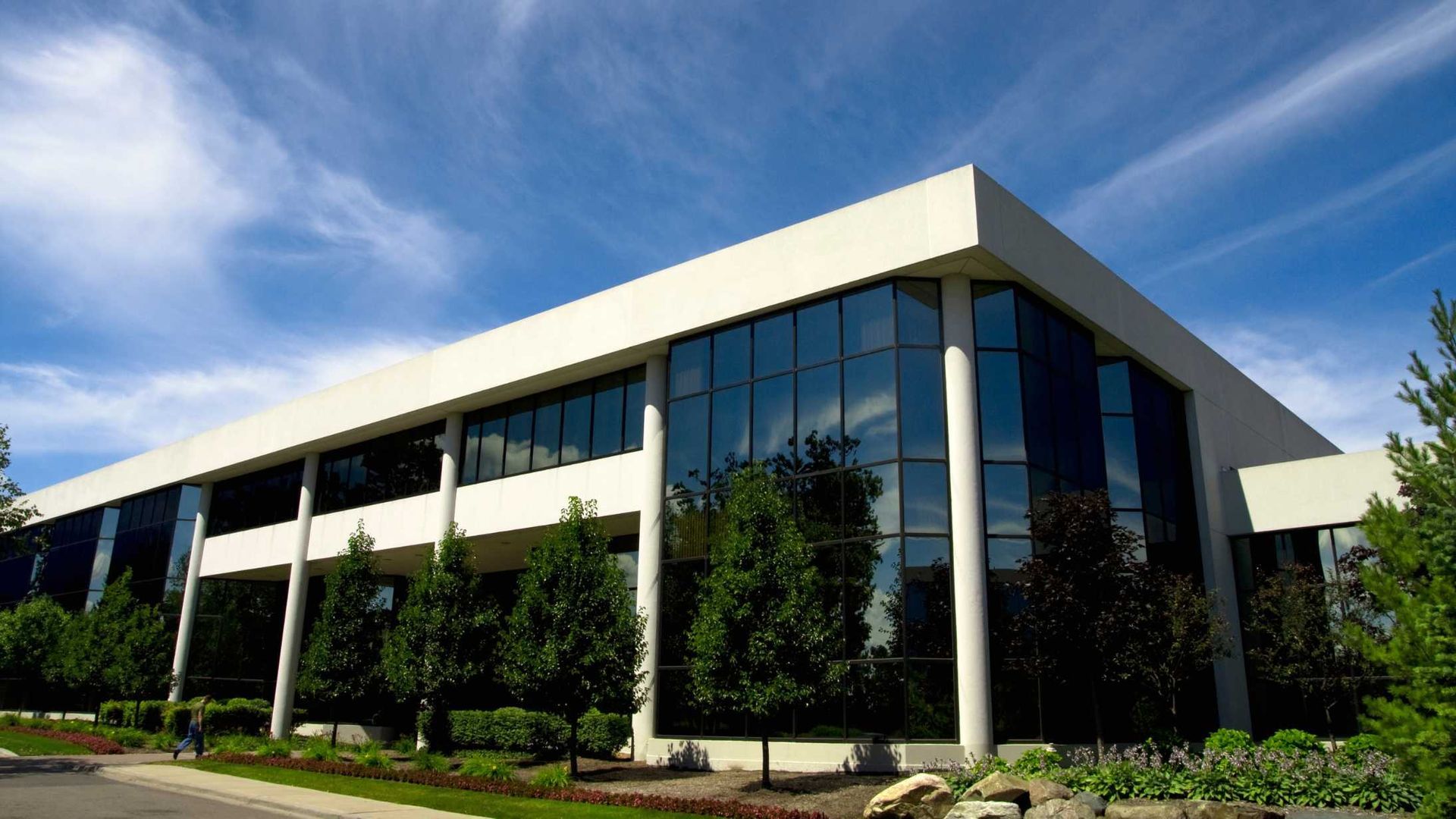 Modern two-story office building with large glass windows and blue sky.