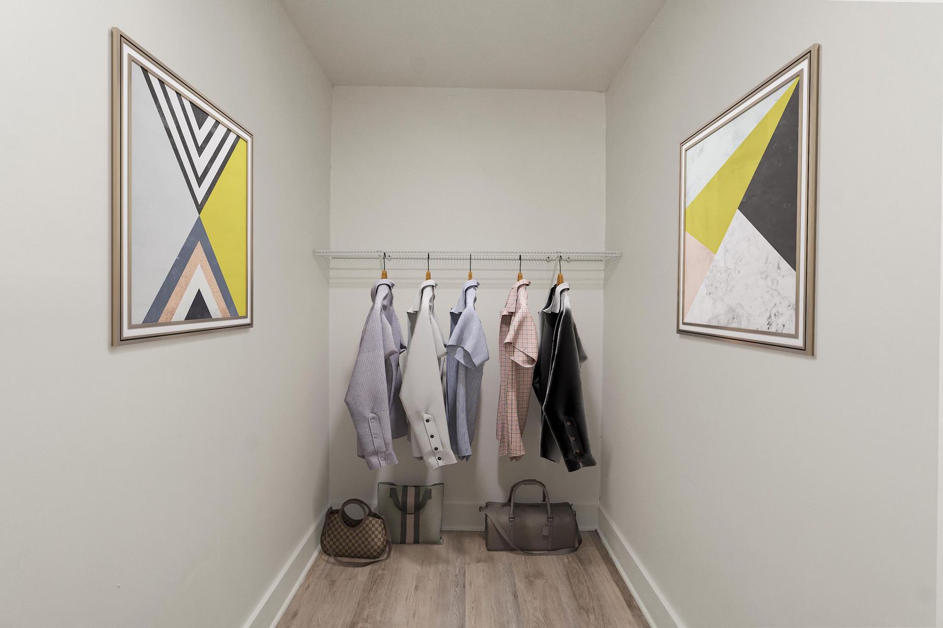 A walk in closet with clothes hanging on racks and two paintings on the wall.