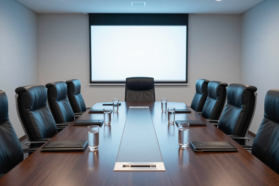 Empty conference room with a long table, black chairs, and a projector screen