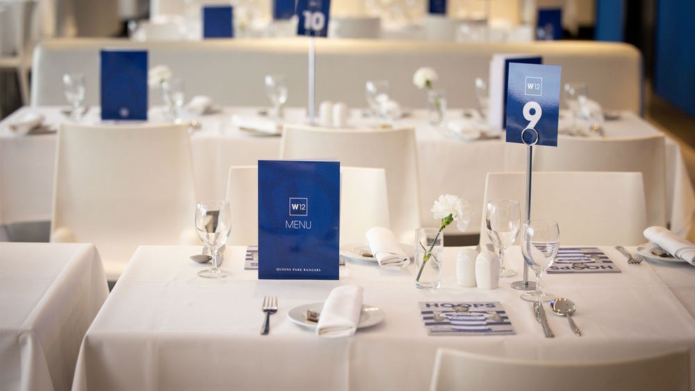 Round banquet tables set with white linens, place settings, and blue table number cards in a formal event hall