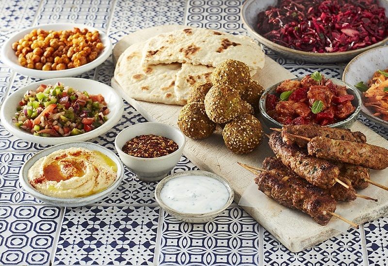 Assorted Middle Eastern dishes on a patterned tablecloth, including flatbread, dips, salads, and grilled meat skewers
