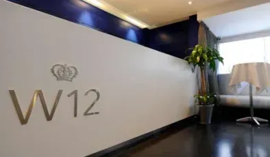 W12 lobby with logo wall, dark wood floor, potted plant, and lamps in a bright hallway