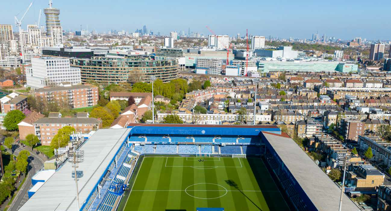 Aerial view of a blue-roofed soccer stadium surrounded by city buildings under a clear sky