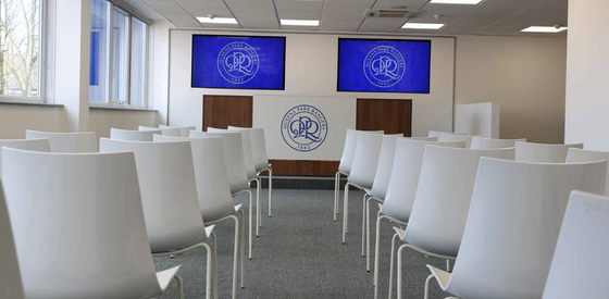 Empty conference room with white chairs facing a podium and presentation screens