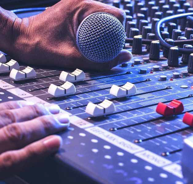 Hands operating an audio mixing console with a microphone resting on it