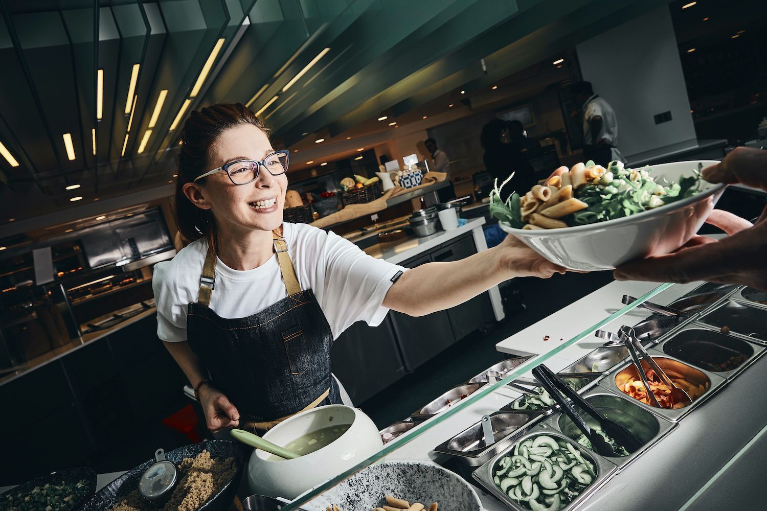 Cafe worker serving a salad bowl at a buffet counter, smiling in a modern restaurant.