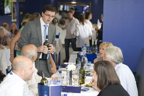 Man speaking at a banquet table with seated guests in a blue-lit conference room