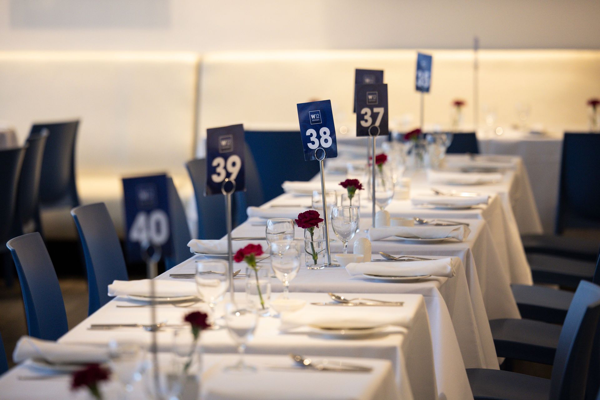 Set dining tables with white cloths, black chairs, and numbered signs in a banquet hall