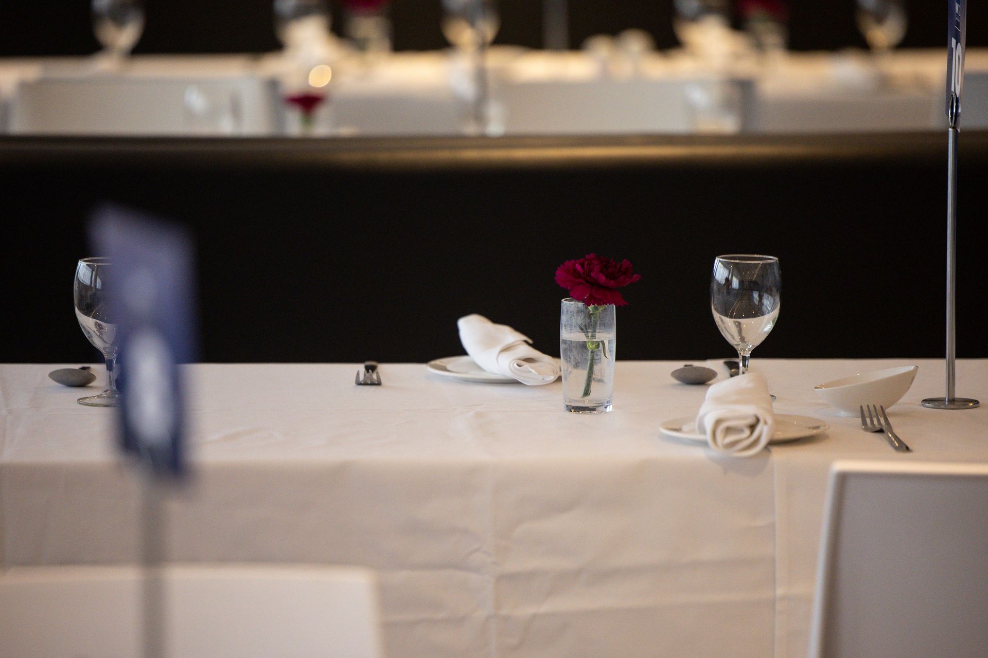 Elegant dining table with white tablecloth, wine glasses, folded napkins, and a red flower centerpiece