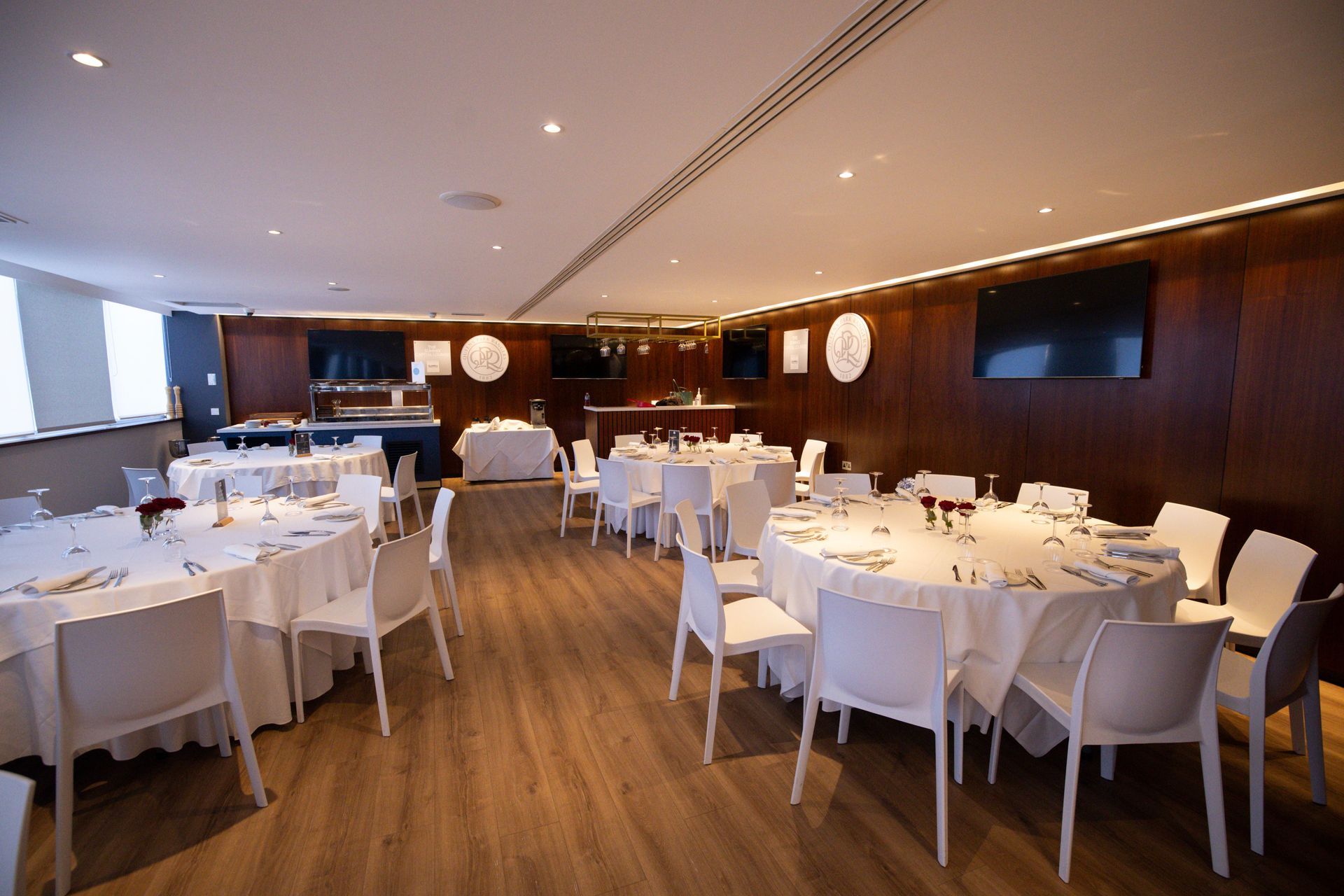 Elegant restaurant dining room with white-clothed tables, white chairs, and warm wood-paneled walls