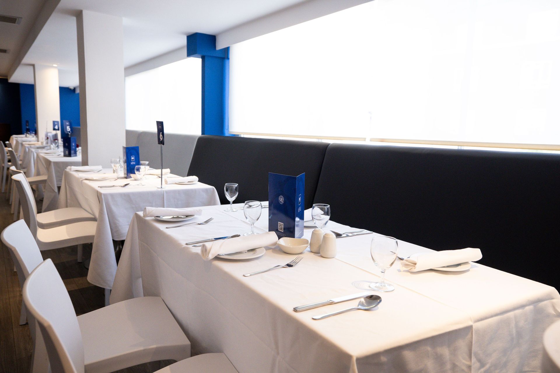 Empty restaurant dining area with white tablecloths, neatly set tables, and blue accent columns