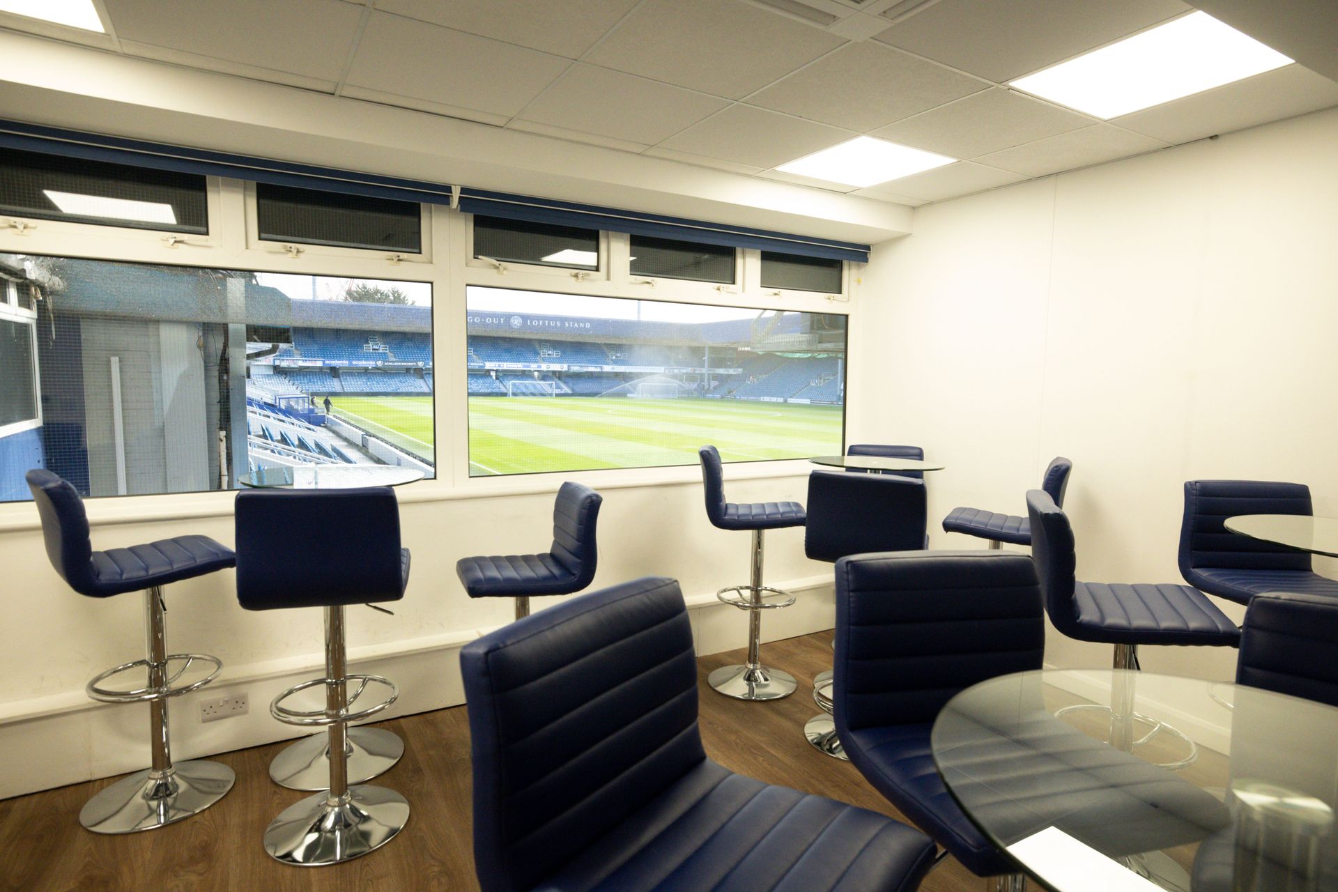 Modern lounge with blue bar stools and chairs overlooking a sports field through large windows