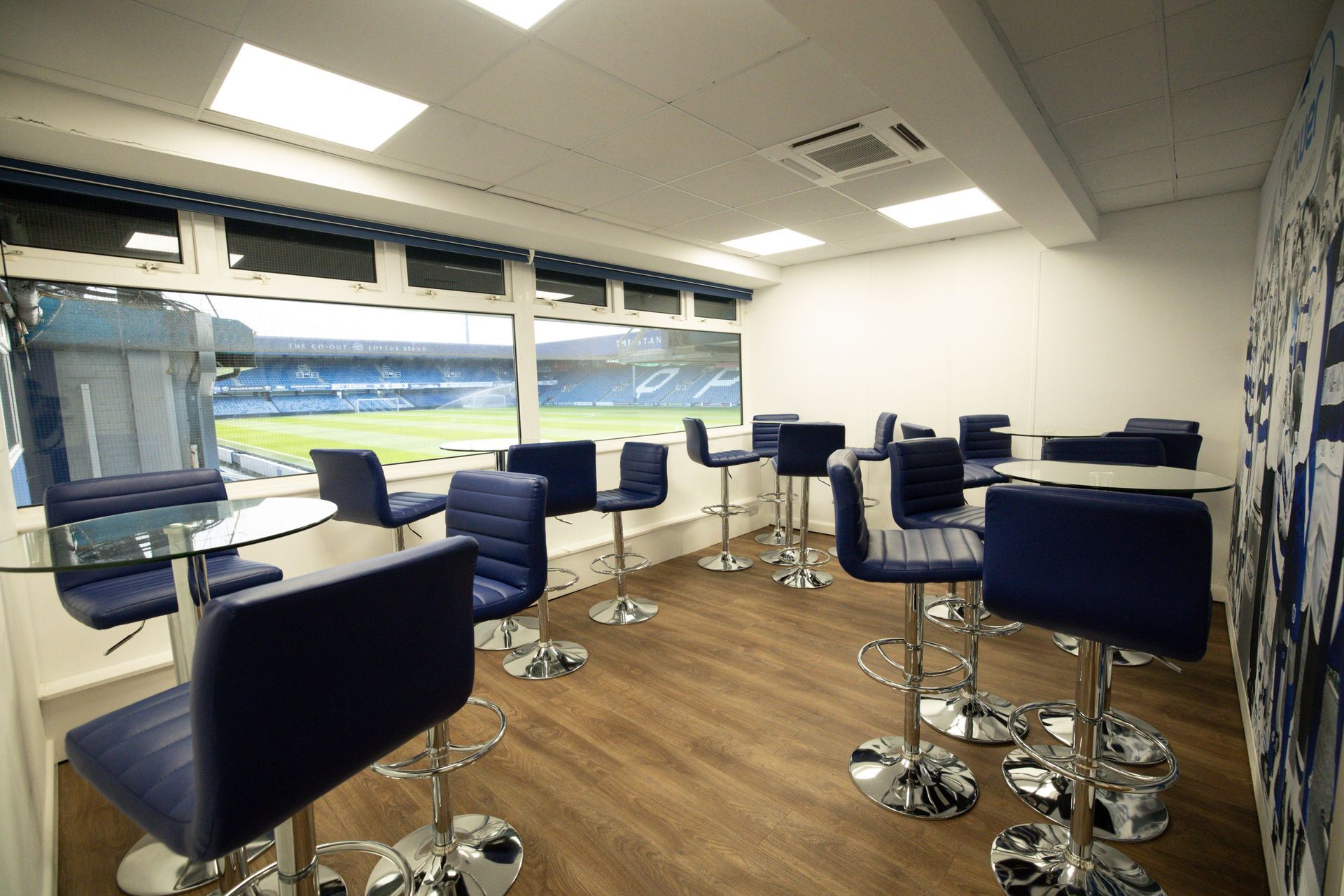 Empty modern lounge with blue stools and chairs beside a large window overlooking a stadium