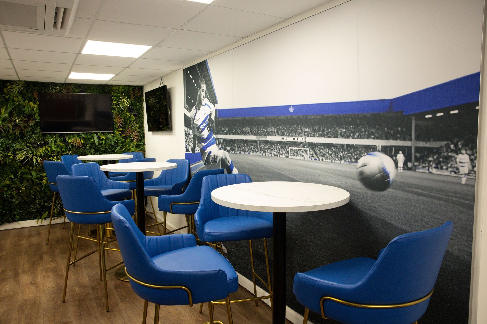 Blue chairs and white tables in a lounge with a black-and-white sports mural on the wall