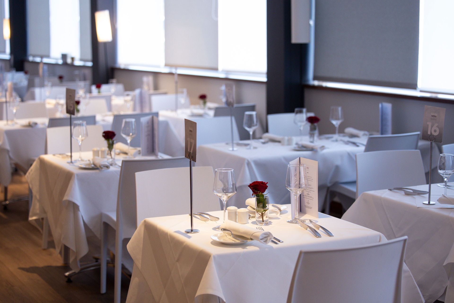Neatly set dining room with white tablecloths, red roses, and soft window light
