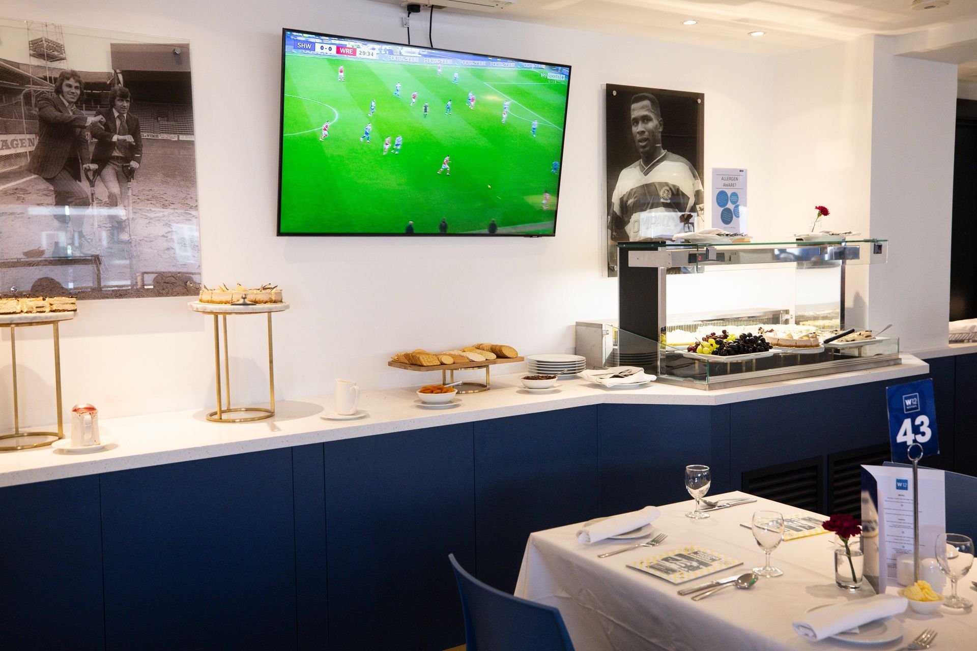Sports bar with a wall-mounted TV showing a soccer match above a buffet table and table settings