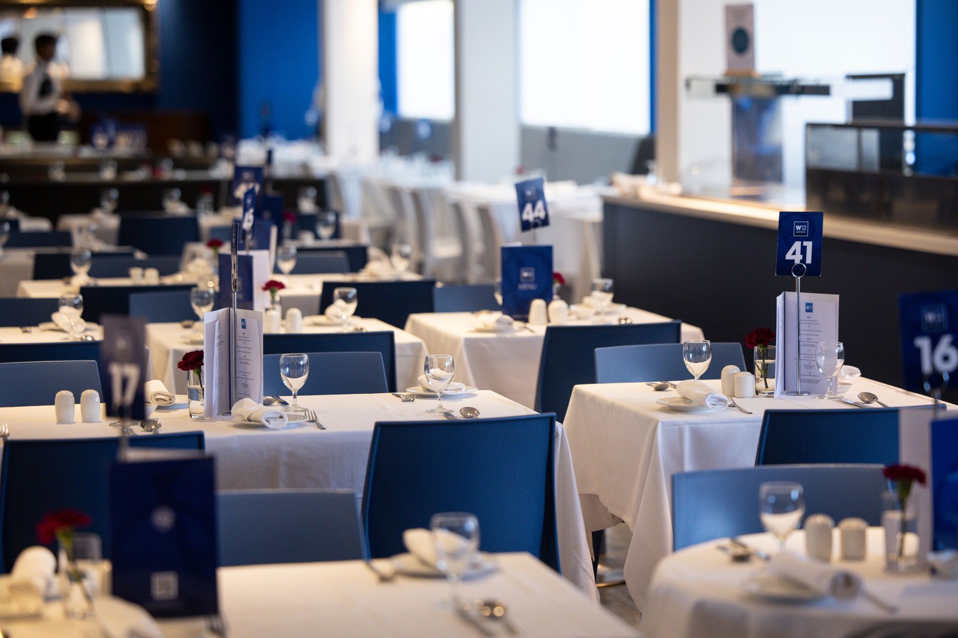Empty restaurant dining room with white tablecloths, blue chairs, and numbered table signs