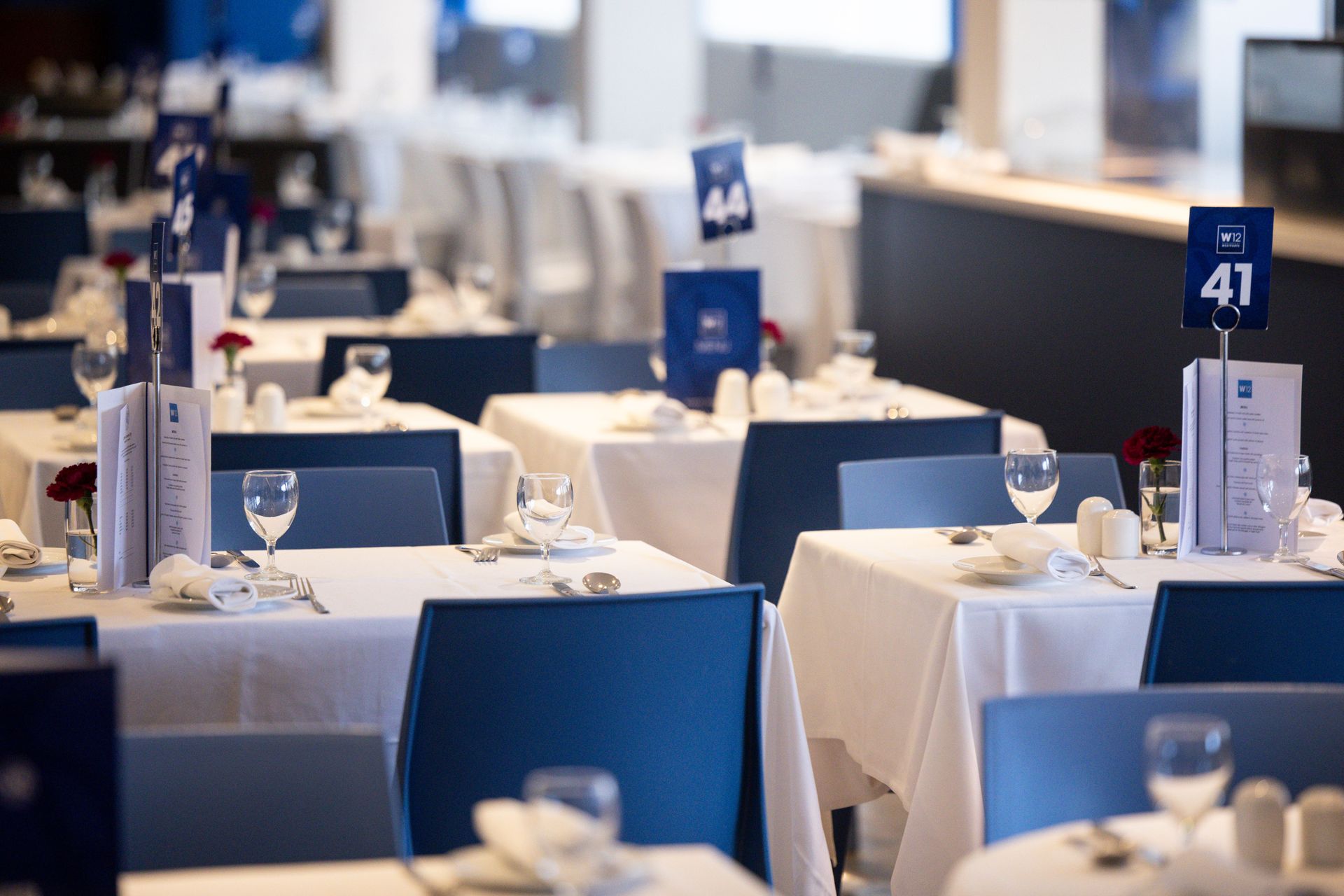 Set dining hall with blue chairs, white tablecloths, and table number signs