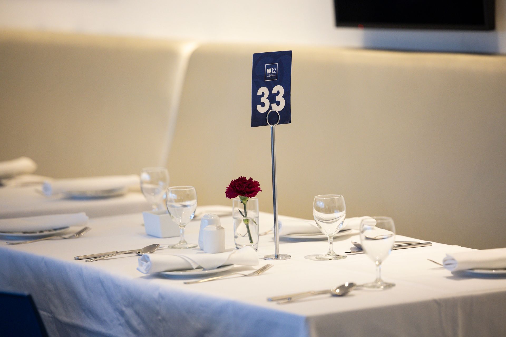 Set dining table with white linens, glassware, red flowers, and table number 33