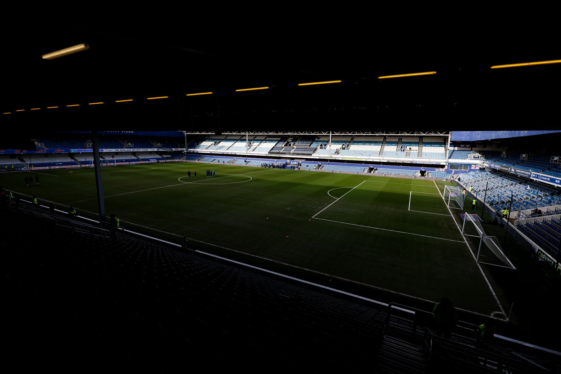Dimly lit soccer stadium at night, with illuminated stands and a green field.