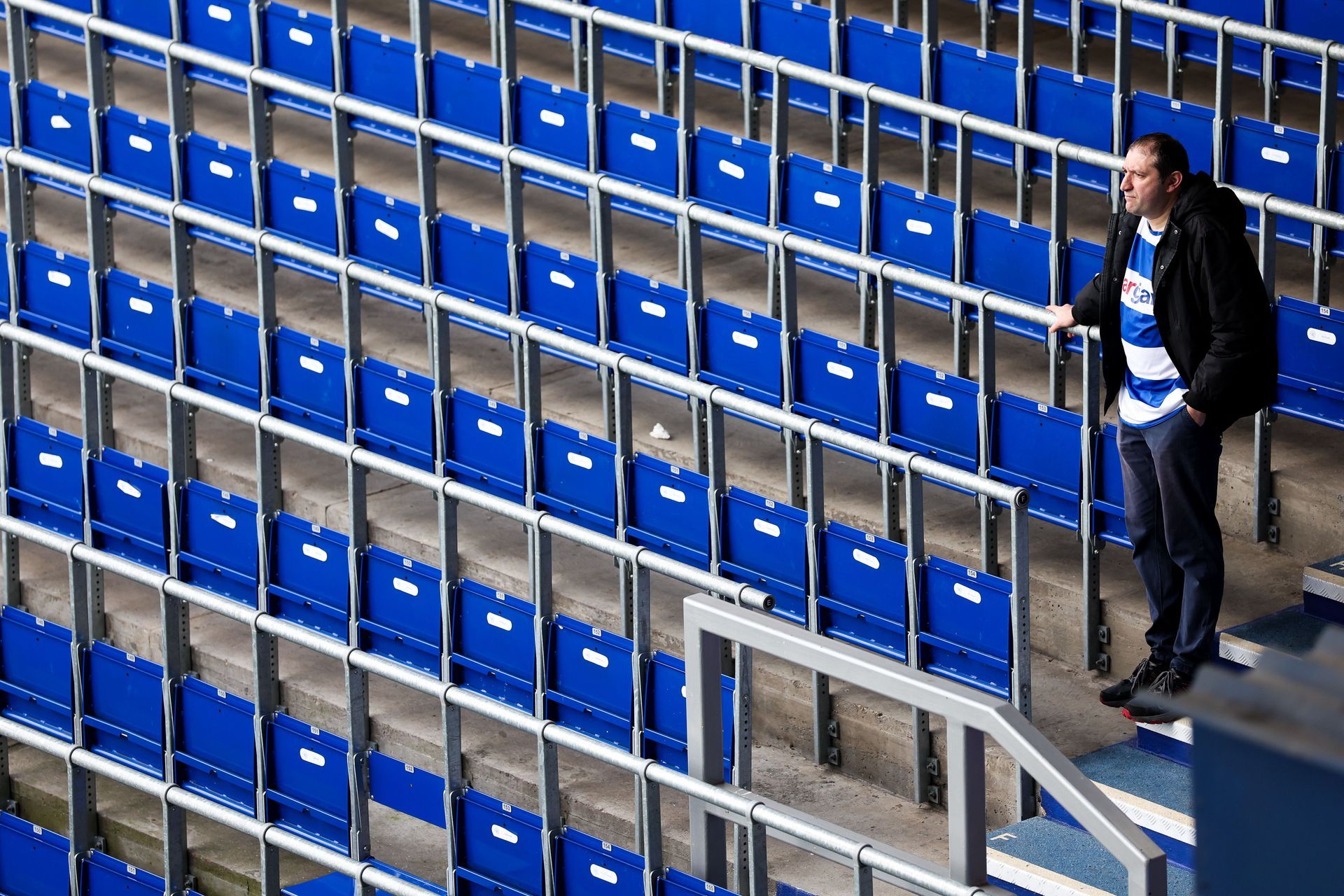 Person walking beside rows of blue stadium seats indoors