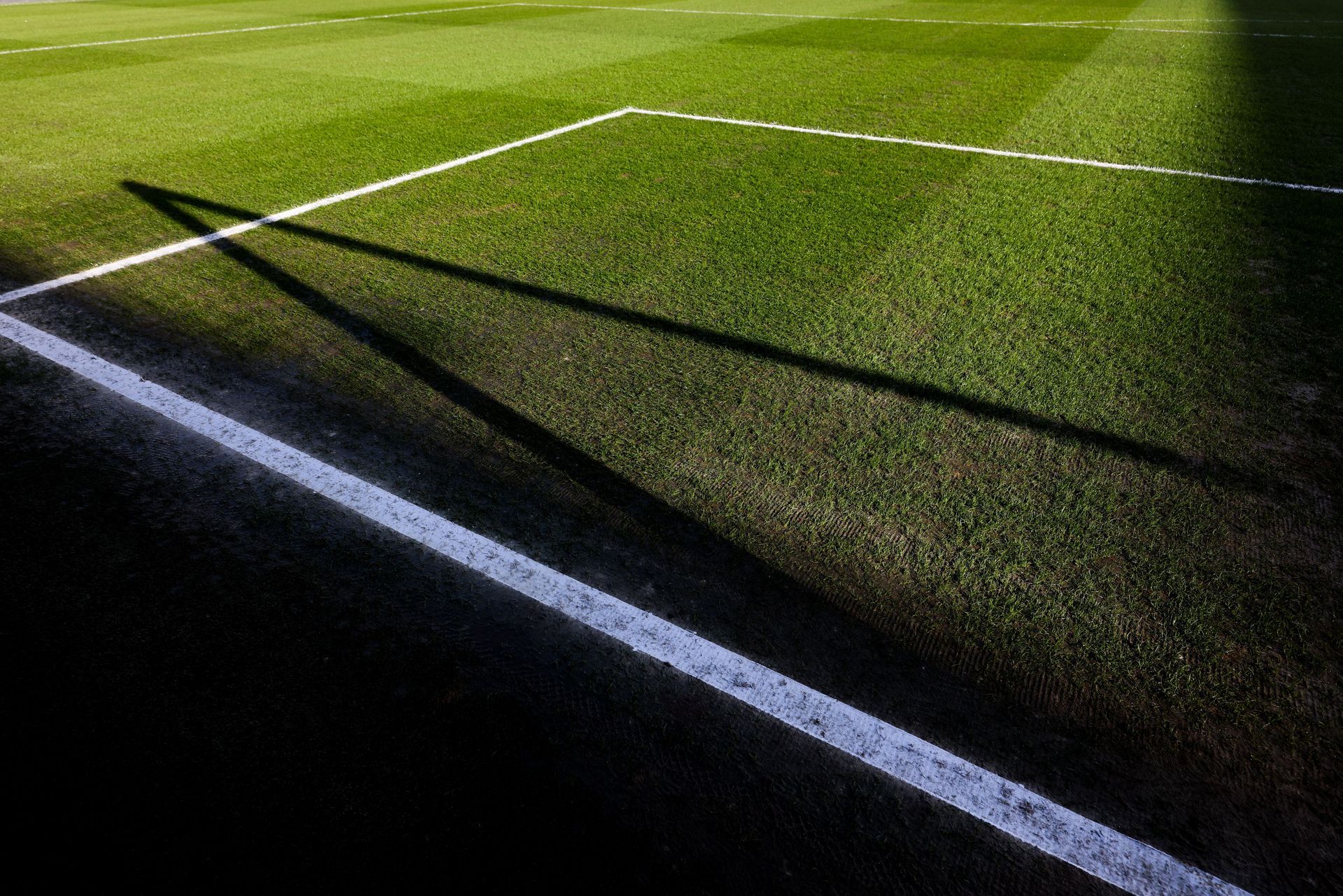 Soccer field corner with white boundary lines on green grass in sunlight
