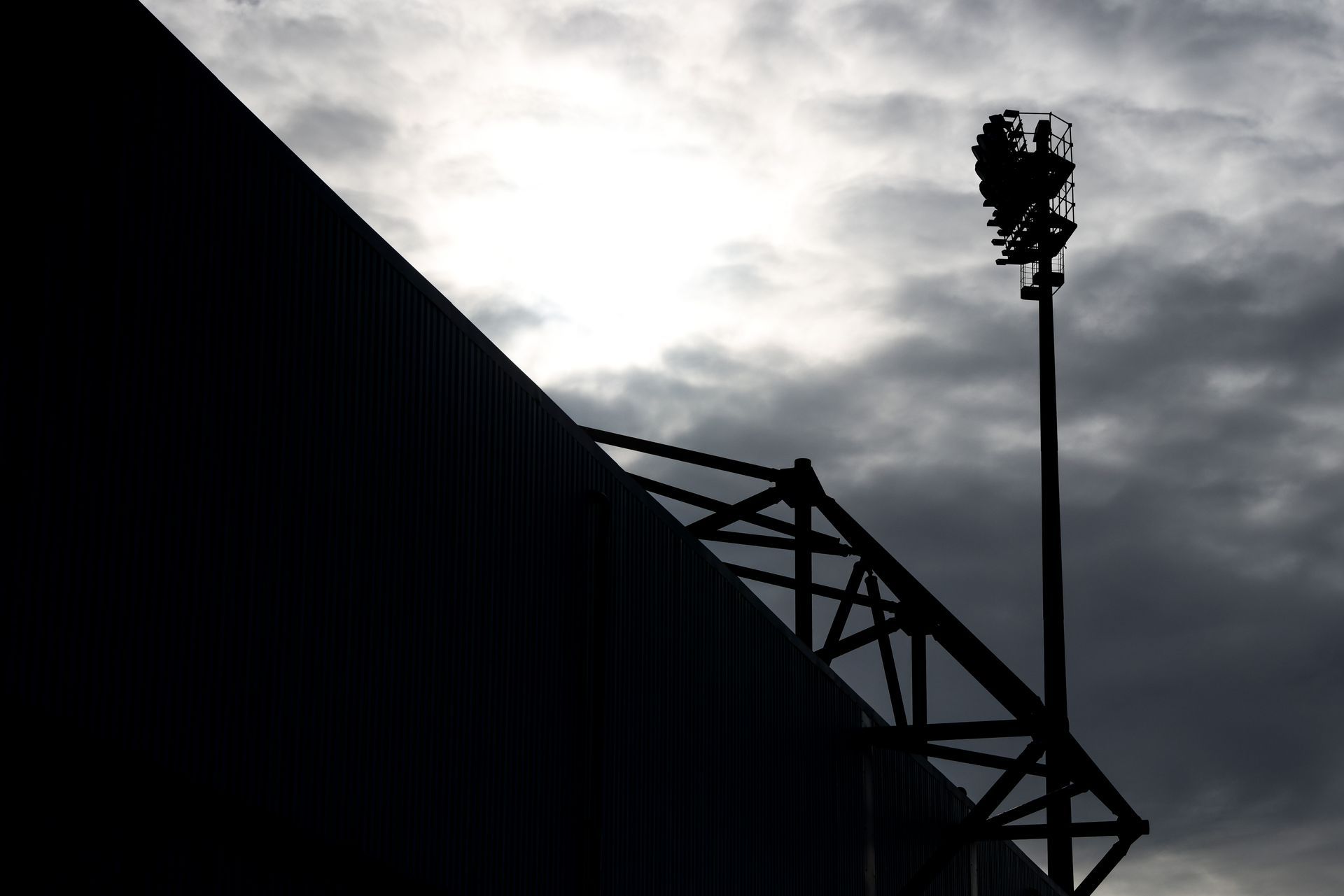 Dark silhouette of a stadium light and roof structure against a cloudy sky