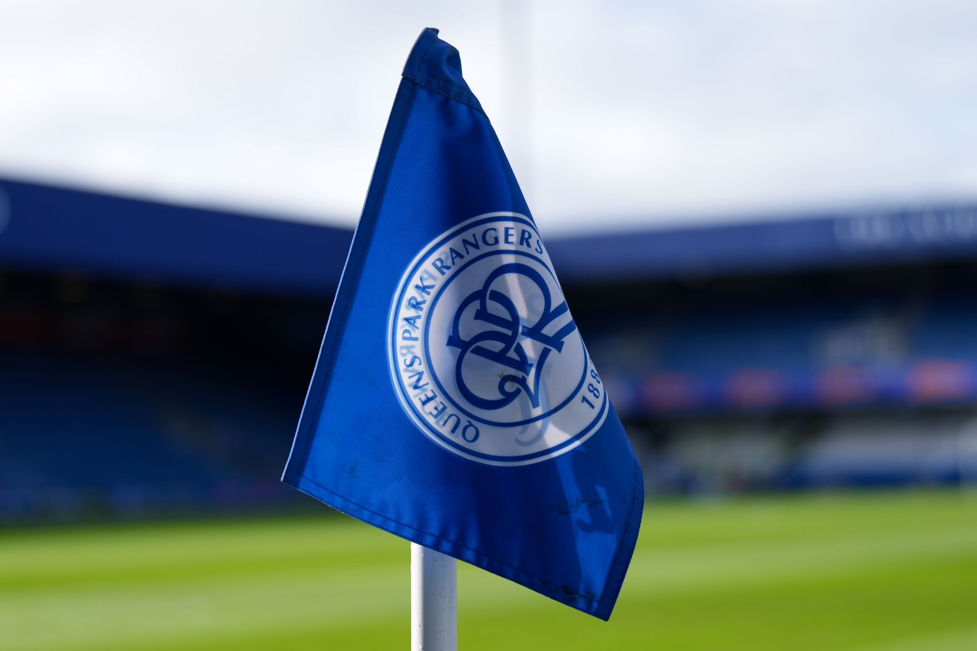 Blue sports corner flag with a circular white club crest on a stadium pitch
