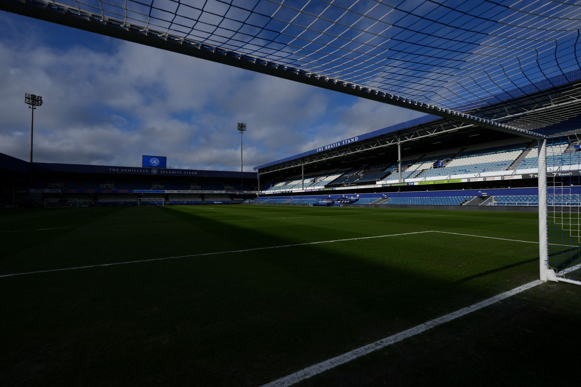 Empty soccer stadium at dusk, viewed from inside the goal under a blue net.