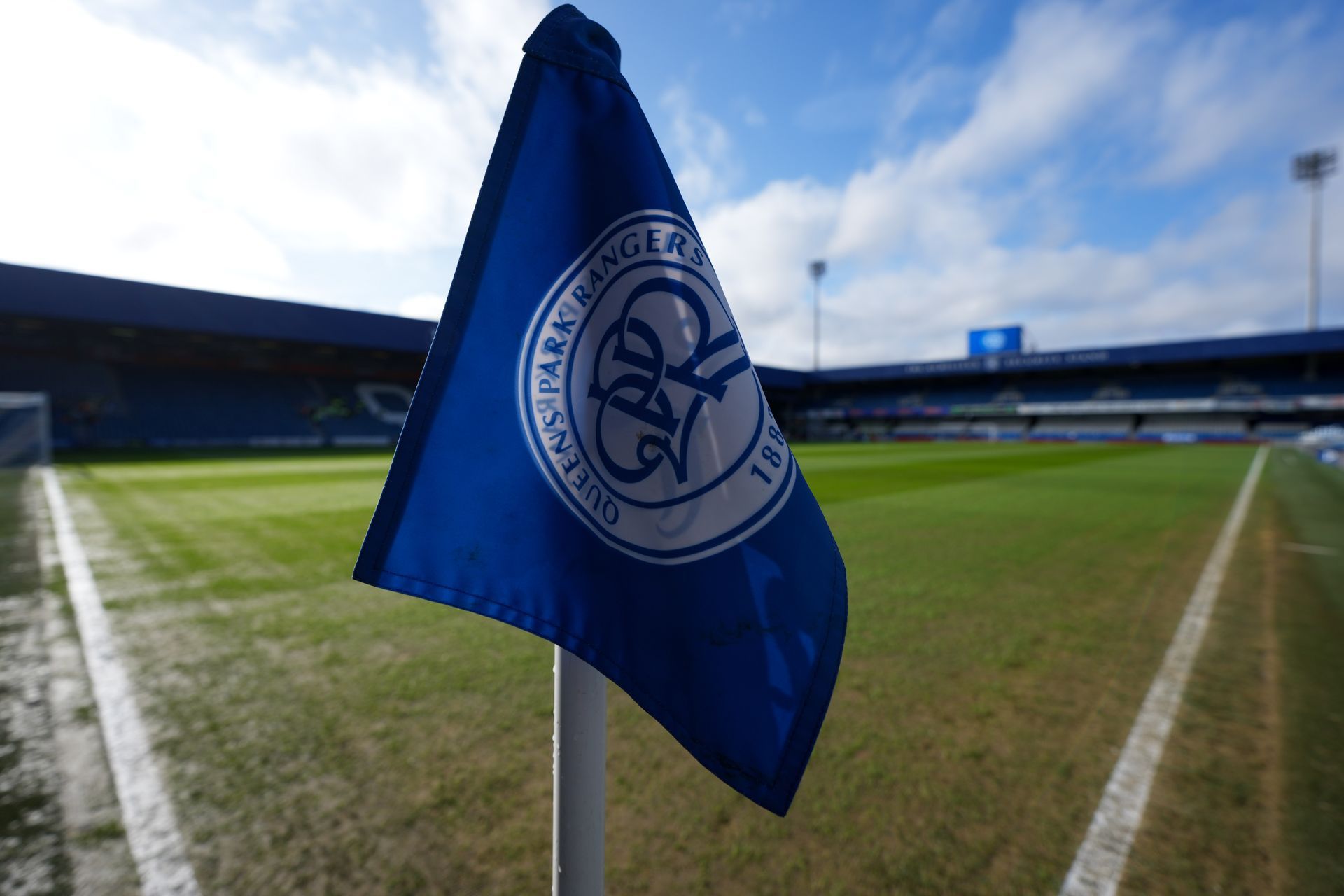 Blue club flag on a soccer field corner, with stadium stands blurred in the background.