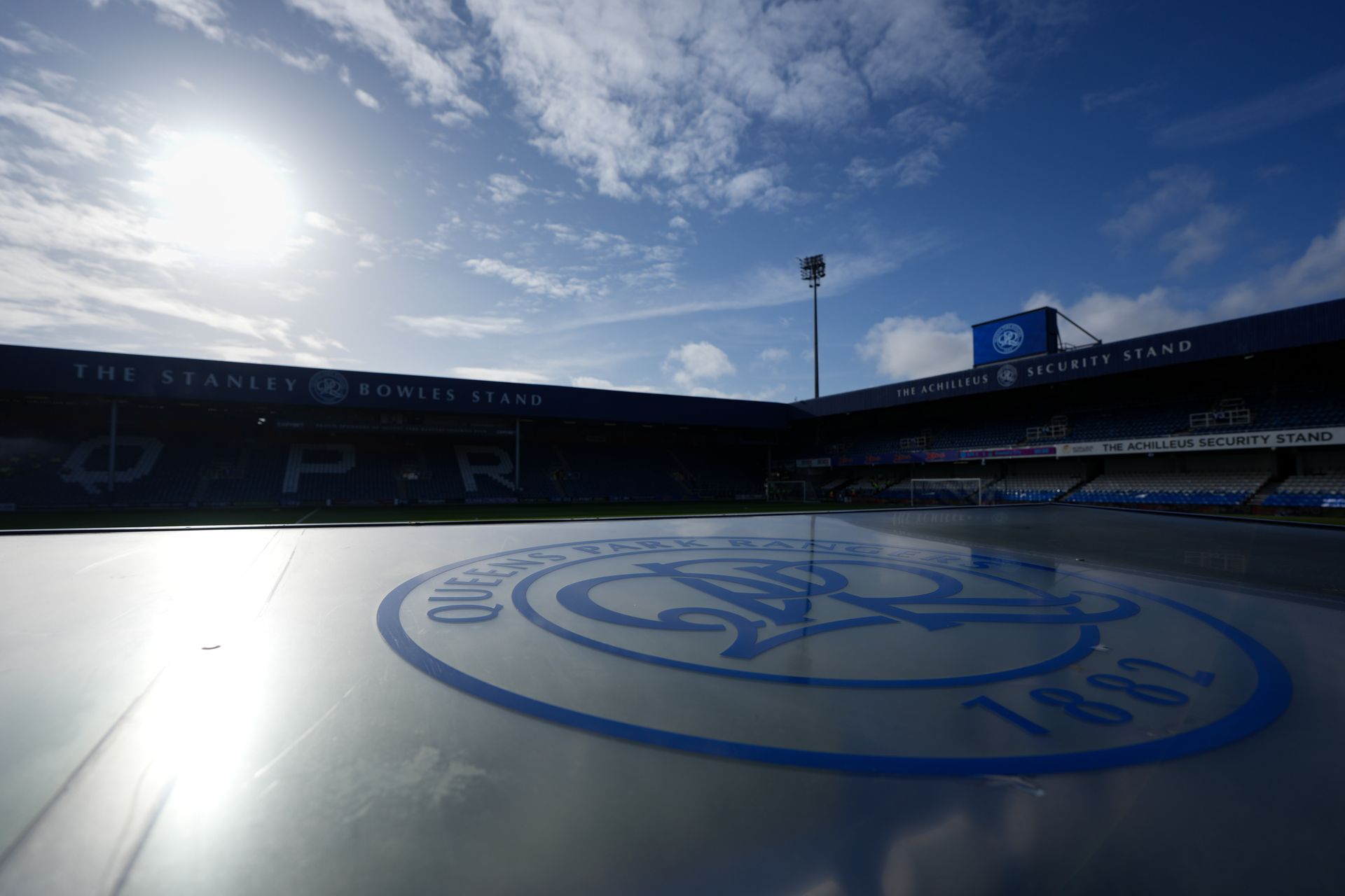 Snowy football stadium under bright sun, with large circular field logo in the foreground.