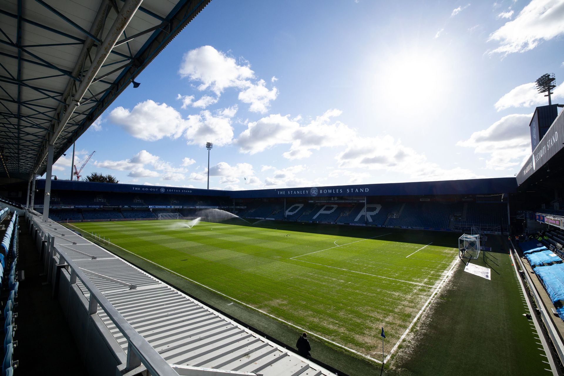 Sunlit empty soccer stadium with green pitch and blue seating stands