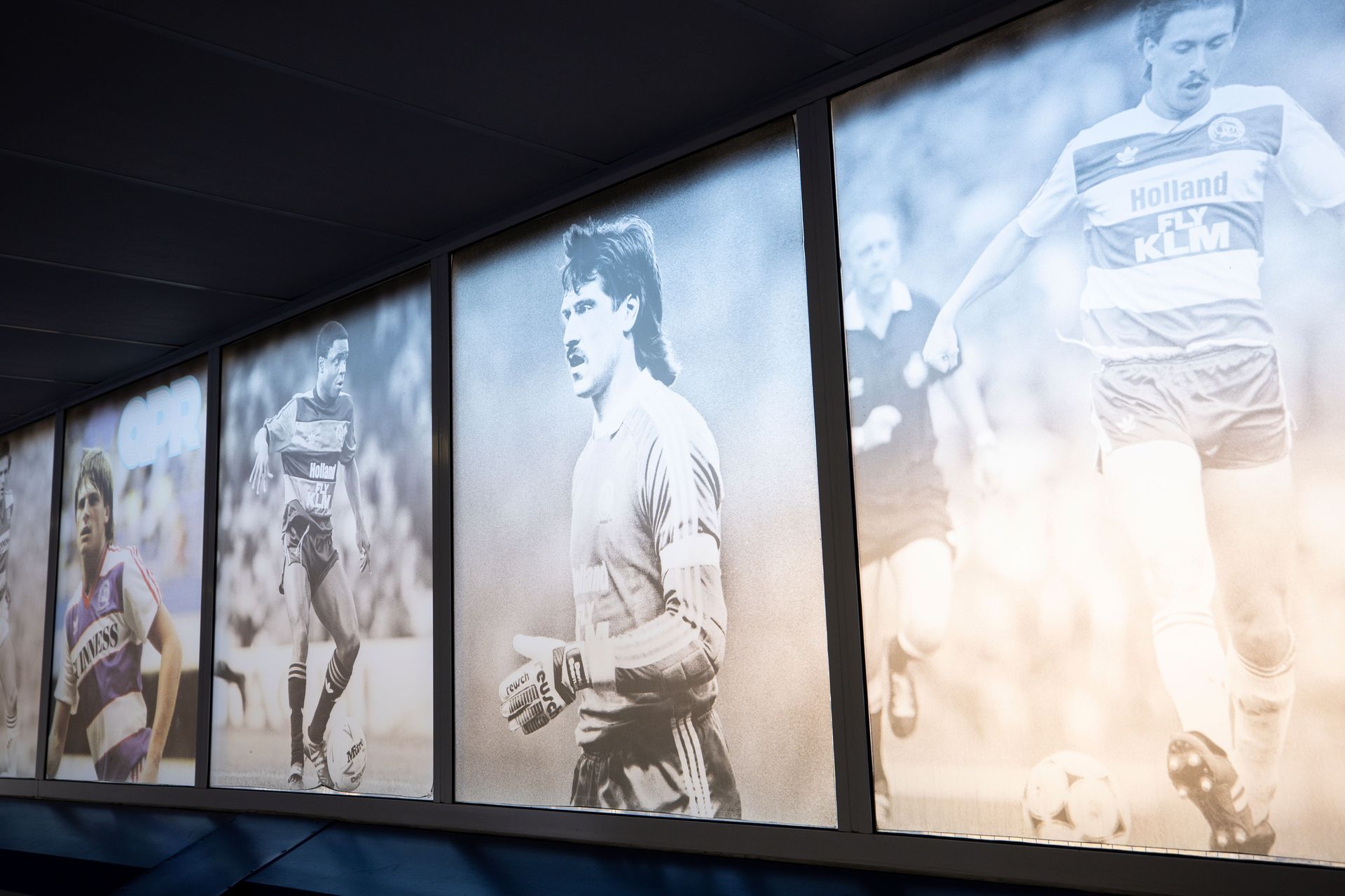 Wall of monochrome athlete portraits in a dim hallway, lit by bright sunlight from the right