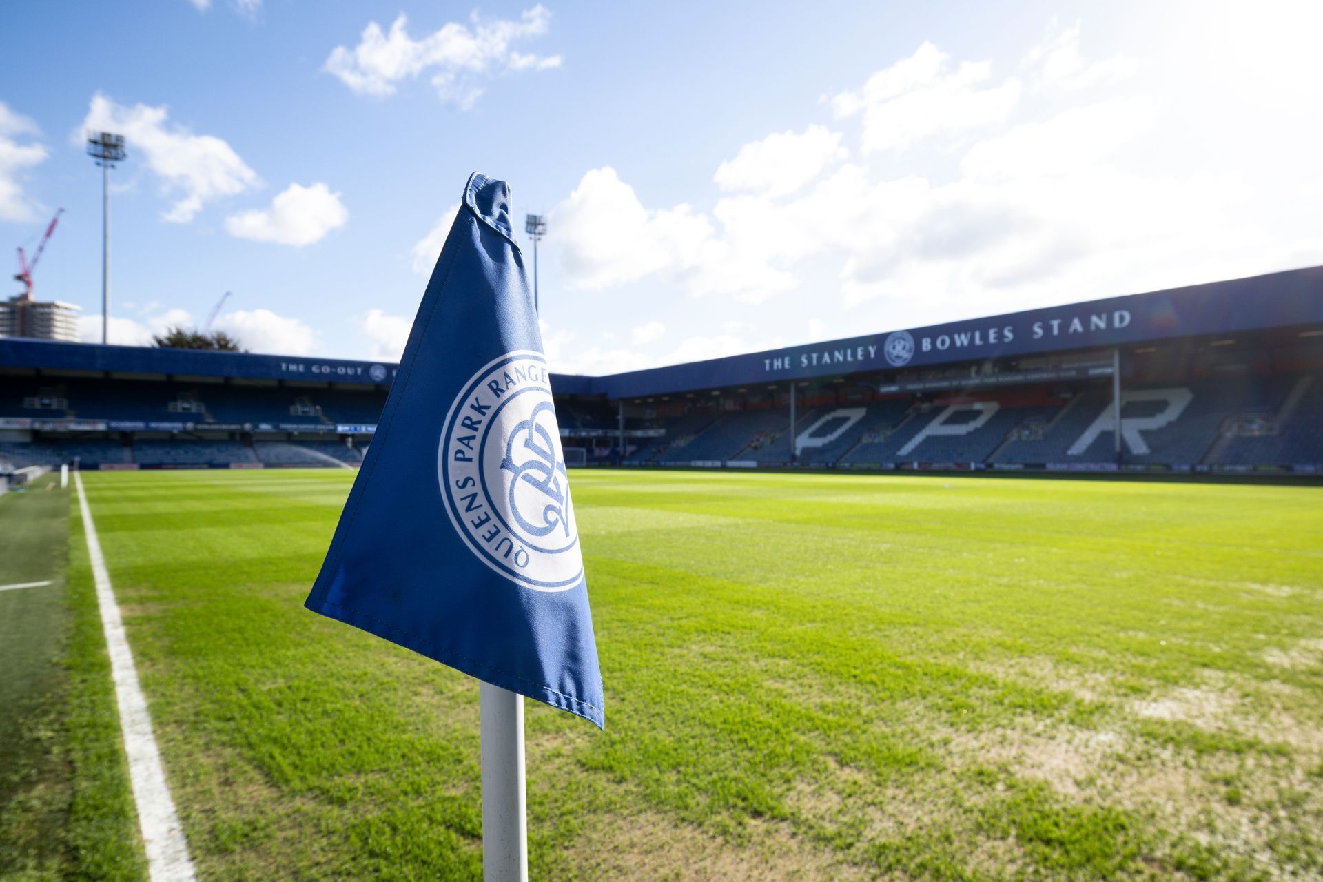 Blue Everton flag on a corner flag post at a sunny football stadium, with green pitch and stands in the background