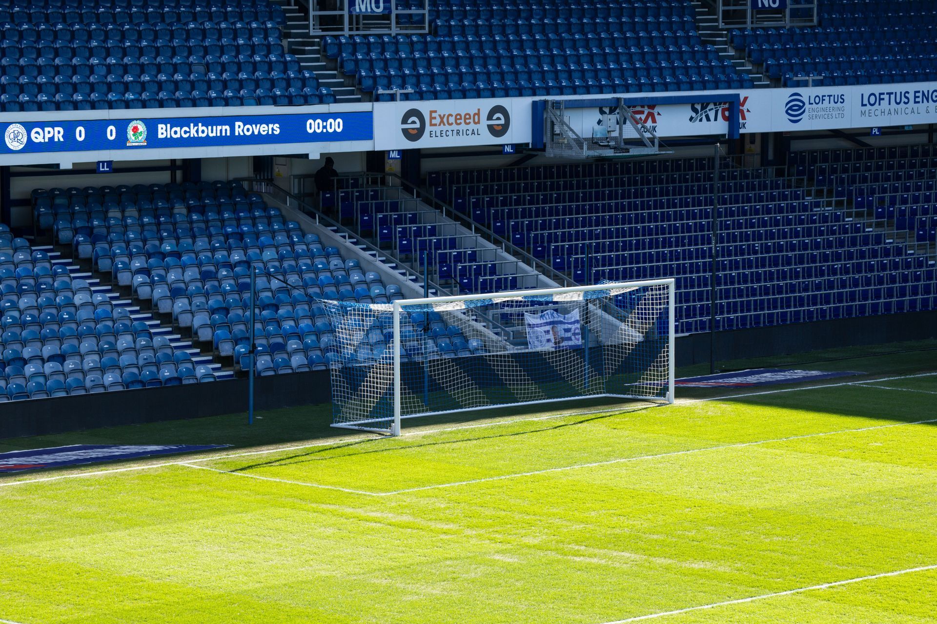 Empty soccer goal on a sunny stadium field with blue seats in the background