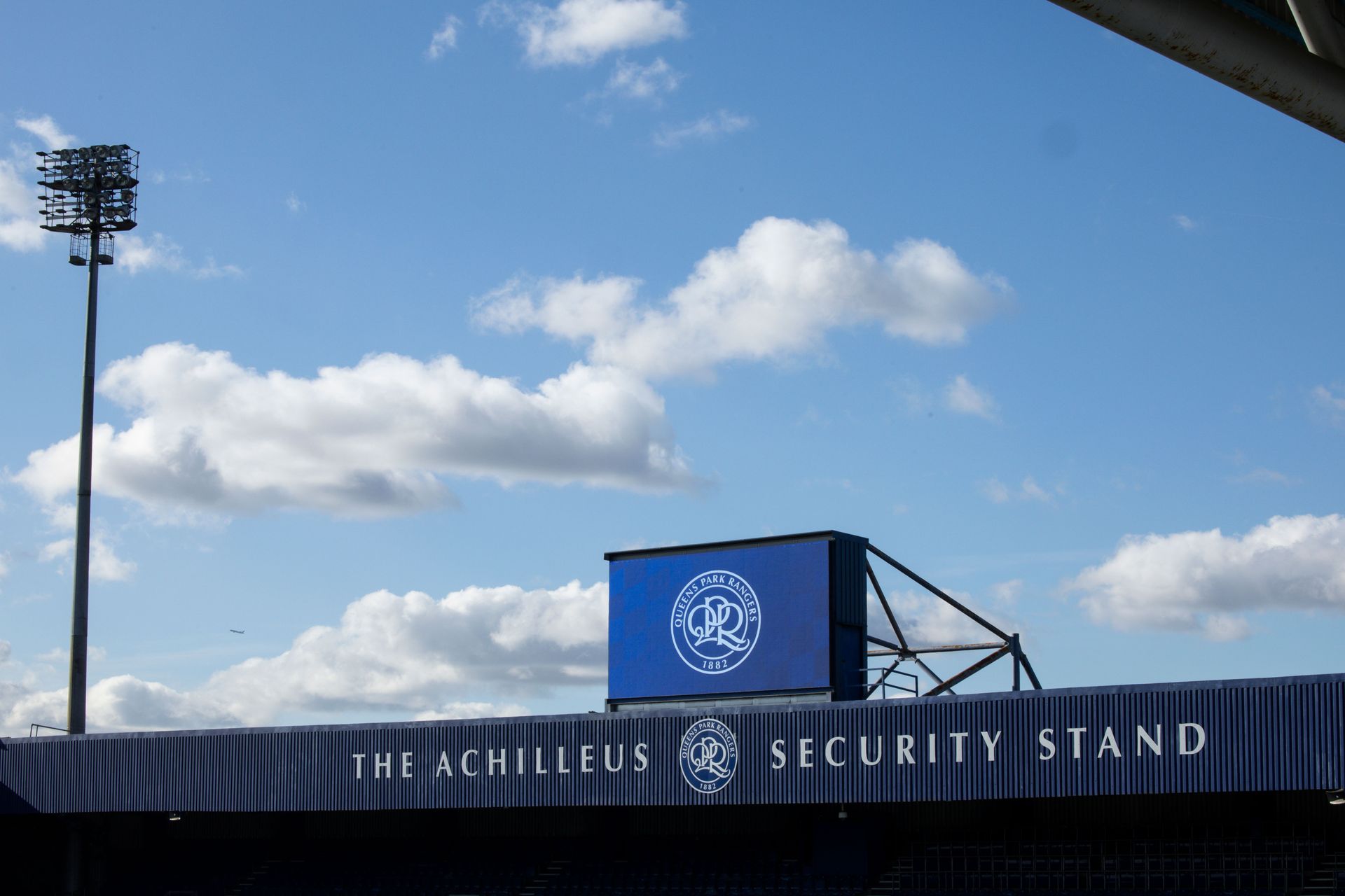 Blue security stand at a stadium under a cloudy sky, with a tall floodlight in the background.