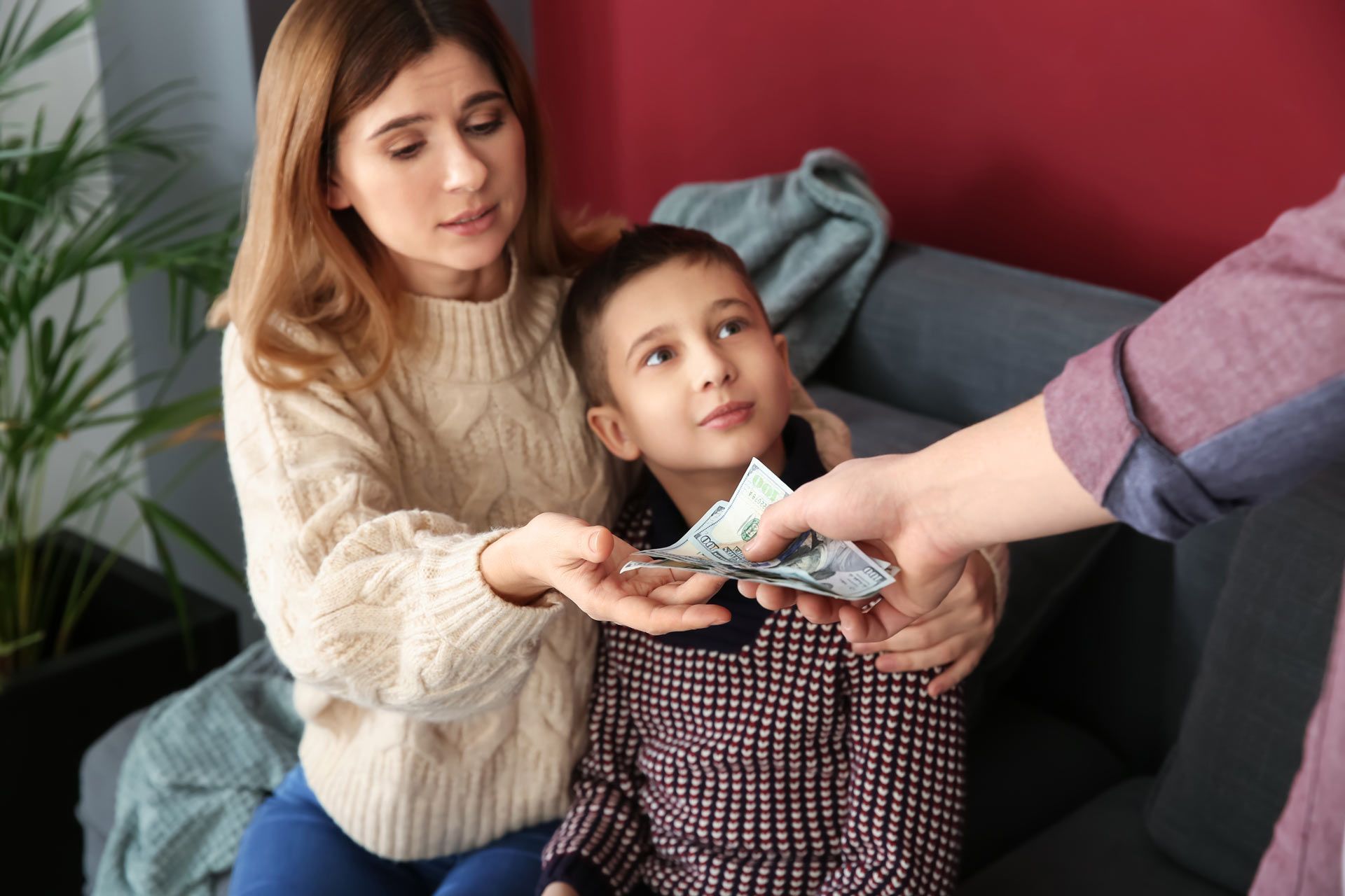 Person giving money to a woman and child on a couch indoors.