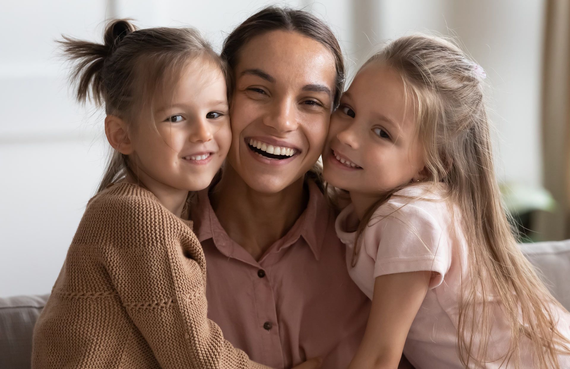 Woman smiling, hugging two children on a couch.