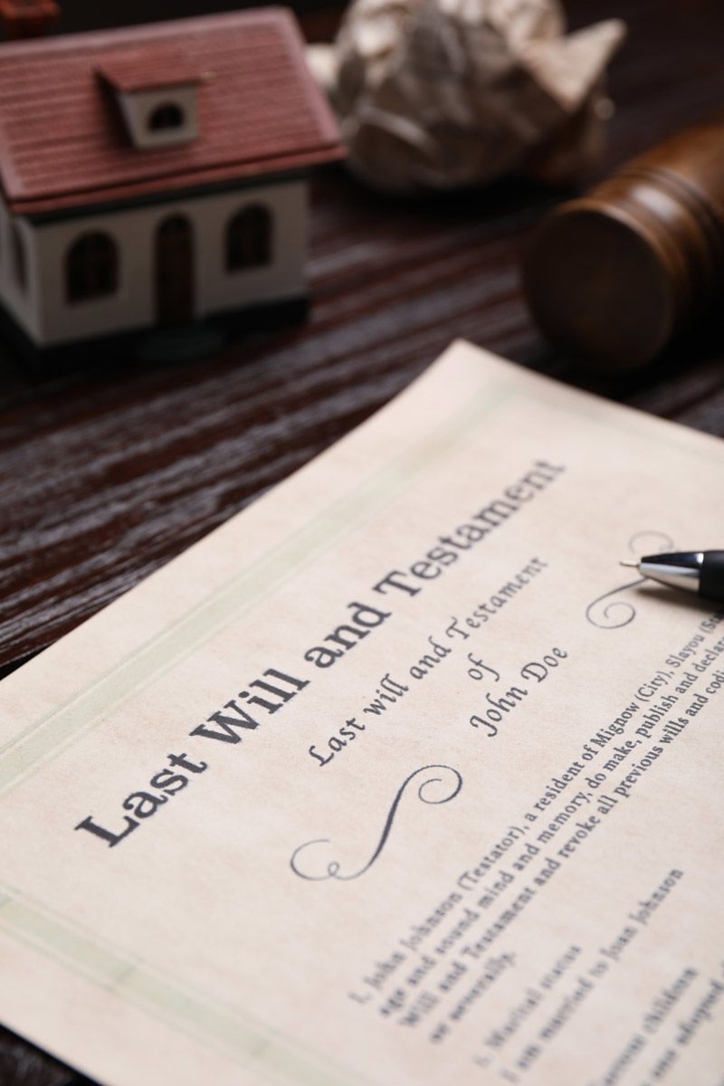 Last Will and Testament document with miniature house and gavel on a wood table.