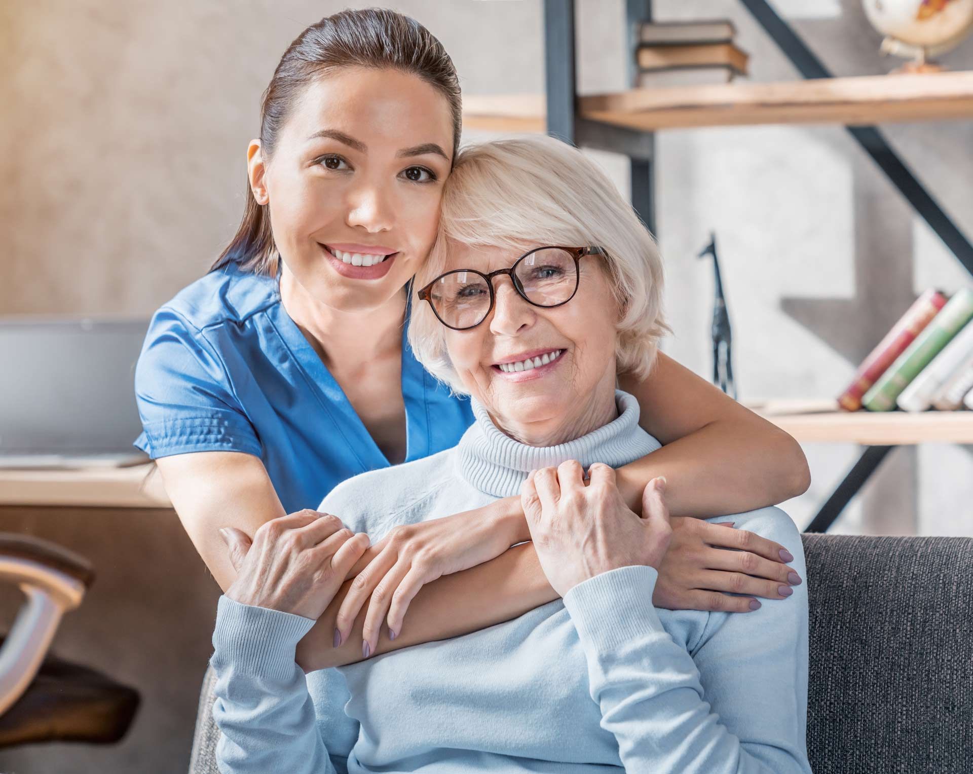Woman hugs an older woman, both smiling, inside a well-lit room.