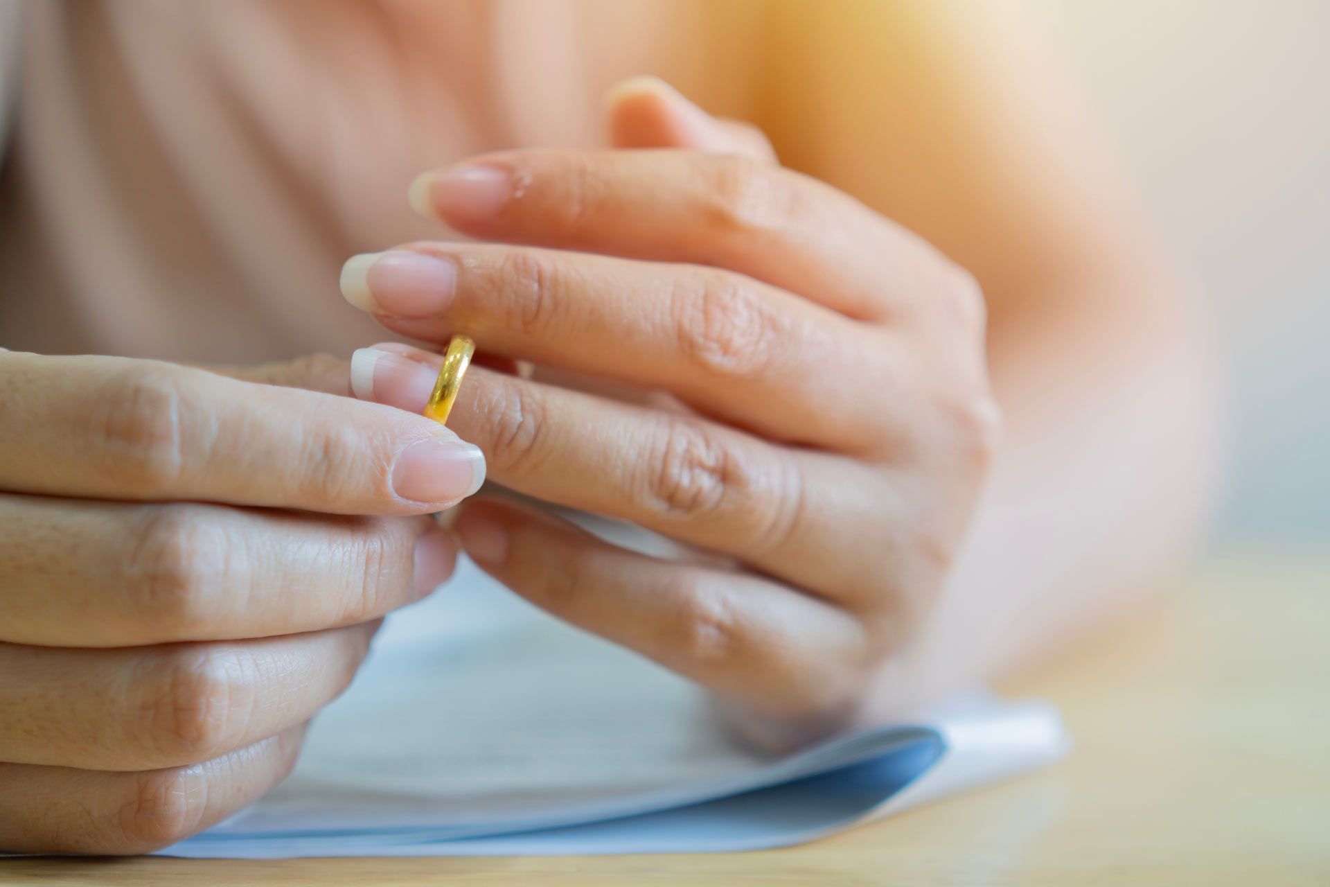 Person removing a gold wedding ring. Focused hands, blurred background.