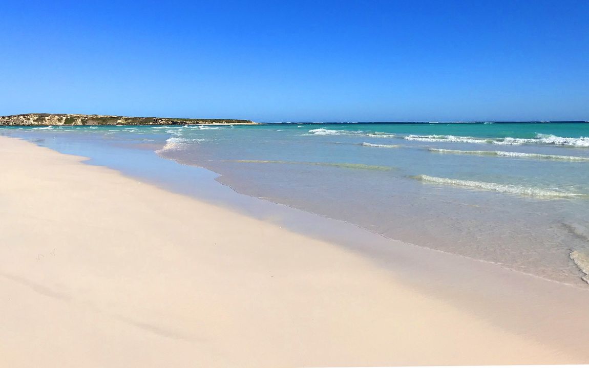 A beach with a lot of sand and waves on a sunny day.