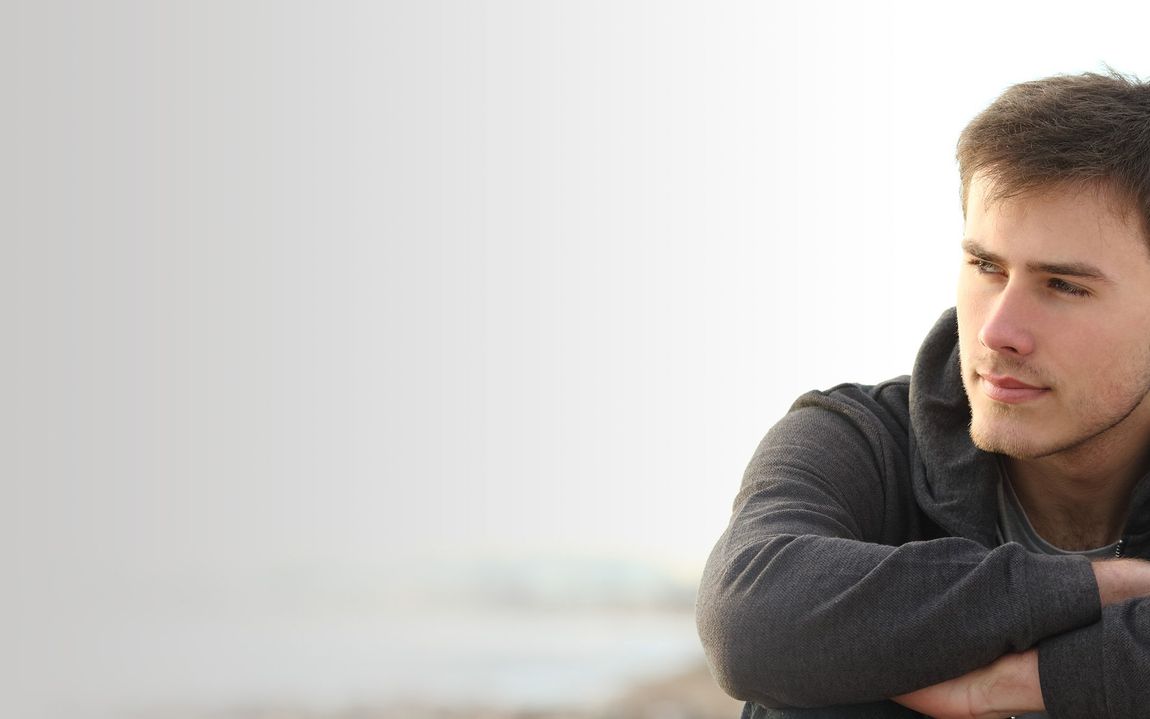 A young man is standing on a beach with his arms crossed.
