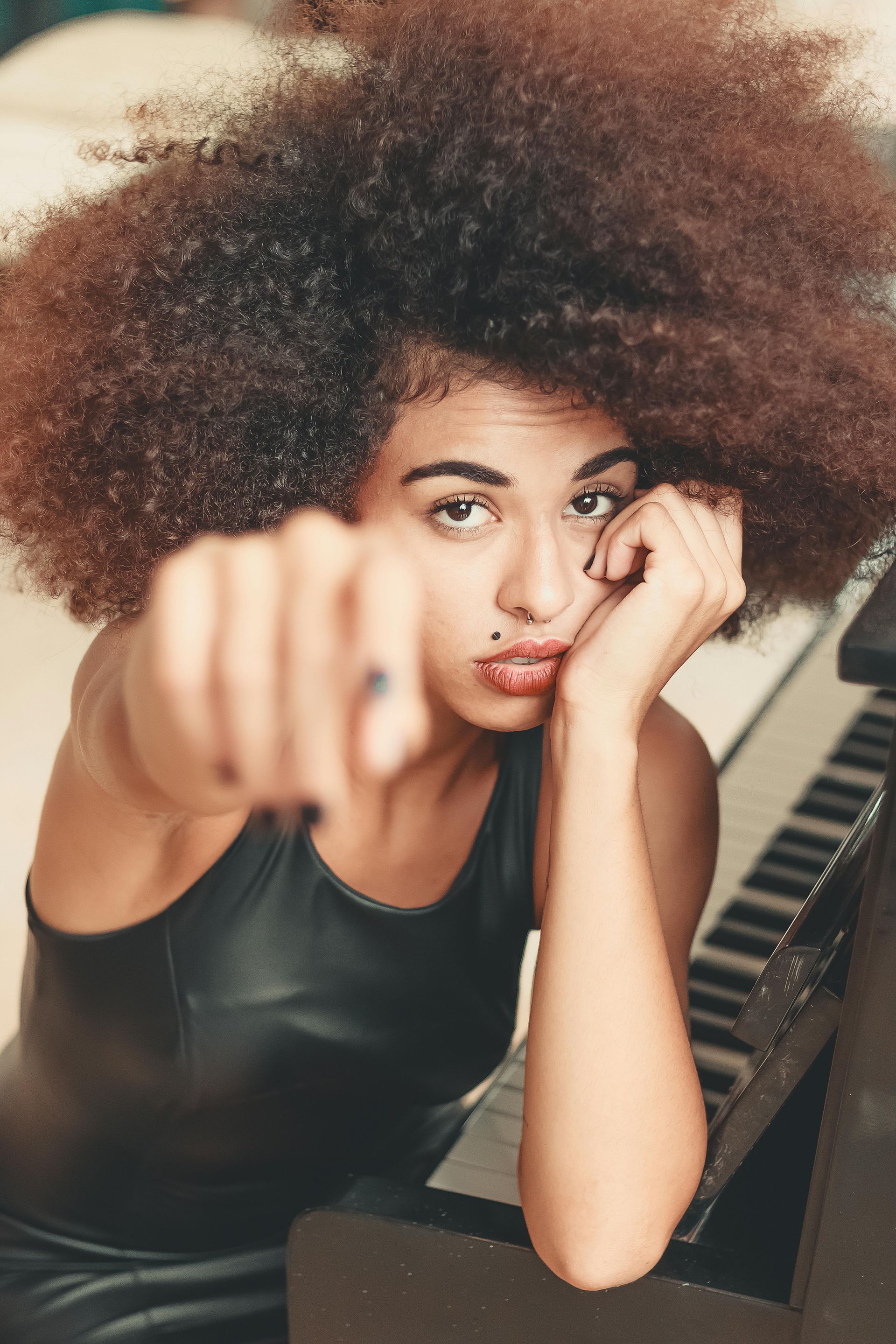 A woman with an afro is sitting at a piano and pointing at the camera.