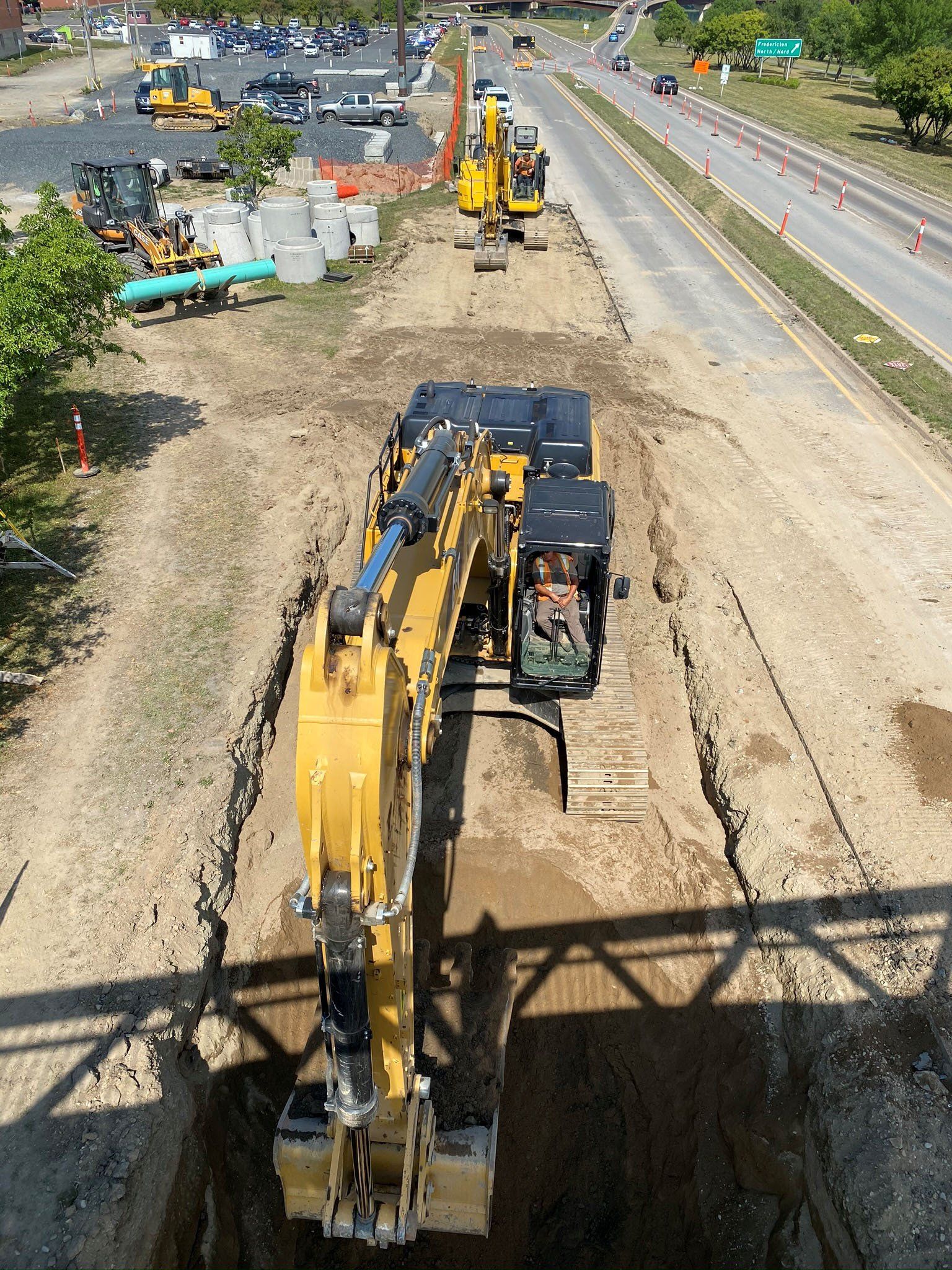 A yellow excavator is digging a hole in the ground next to a road.