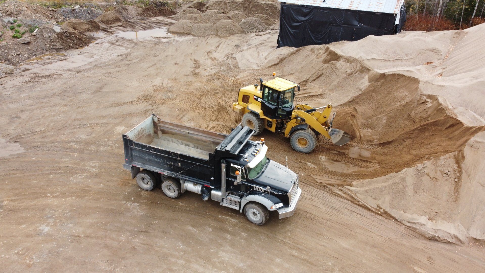 A dump truck is driving down a dirt road next to a bulldozer.