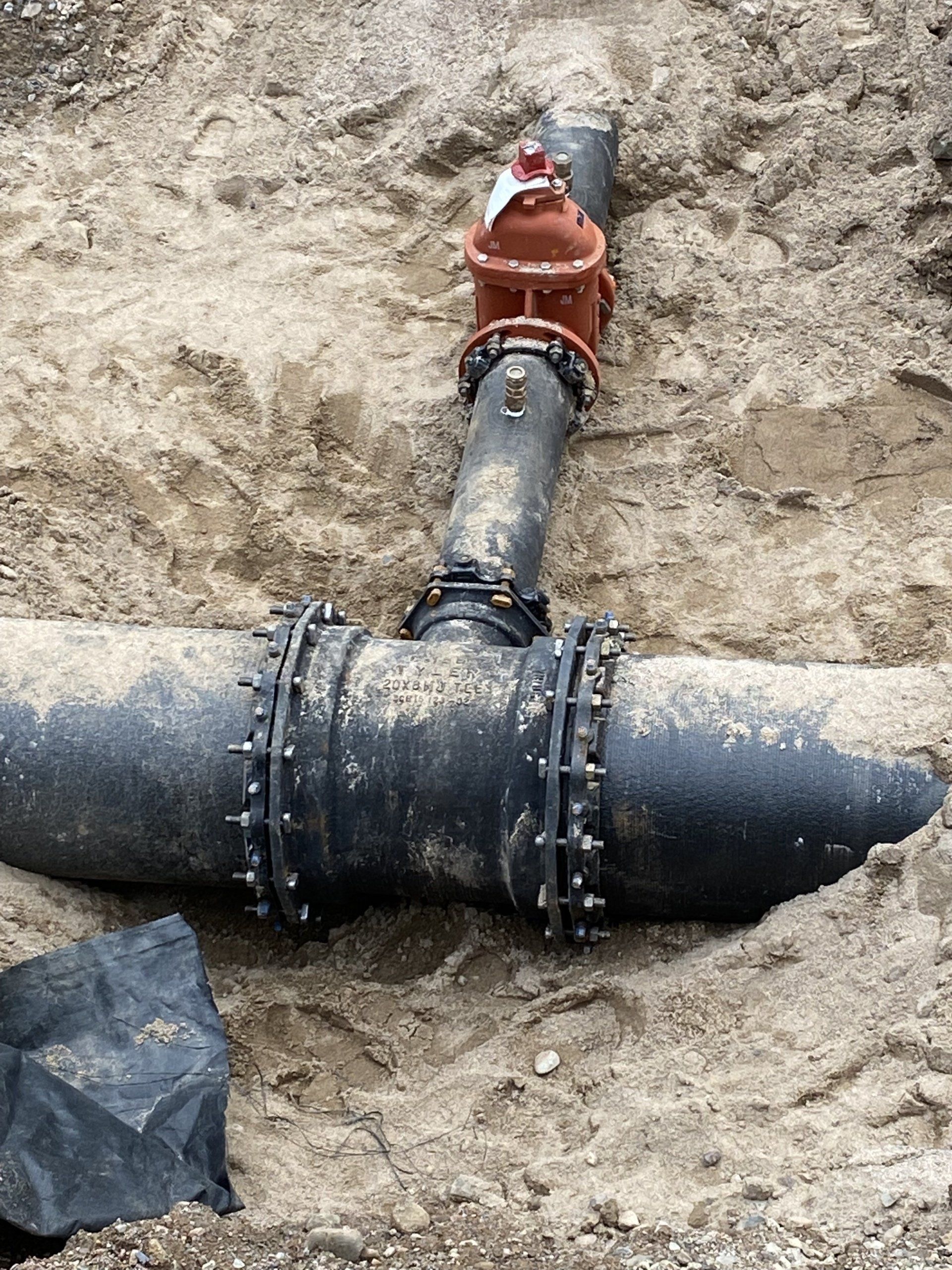 A black pipe with a red valve is laying in the dirt.