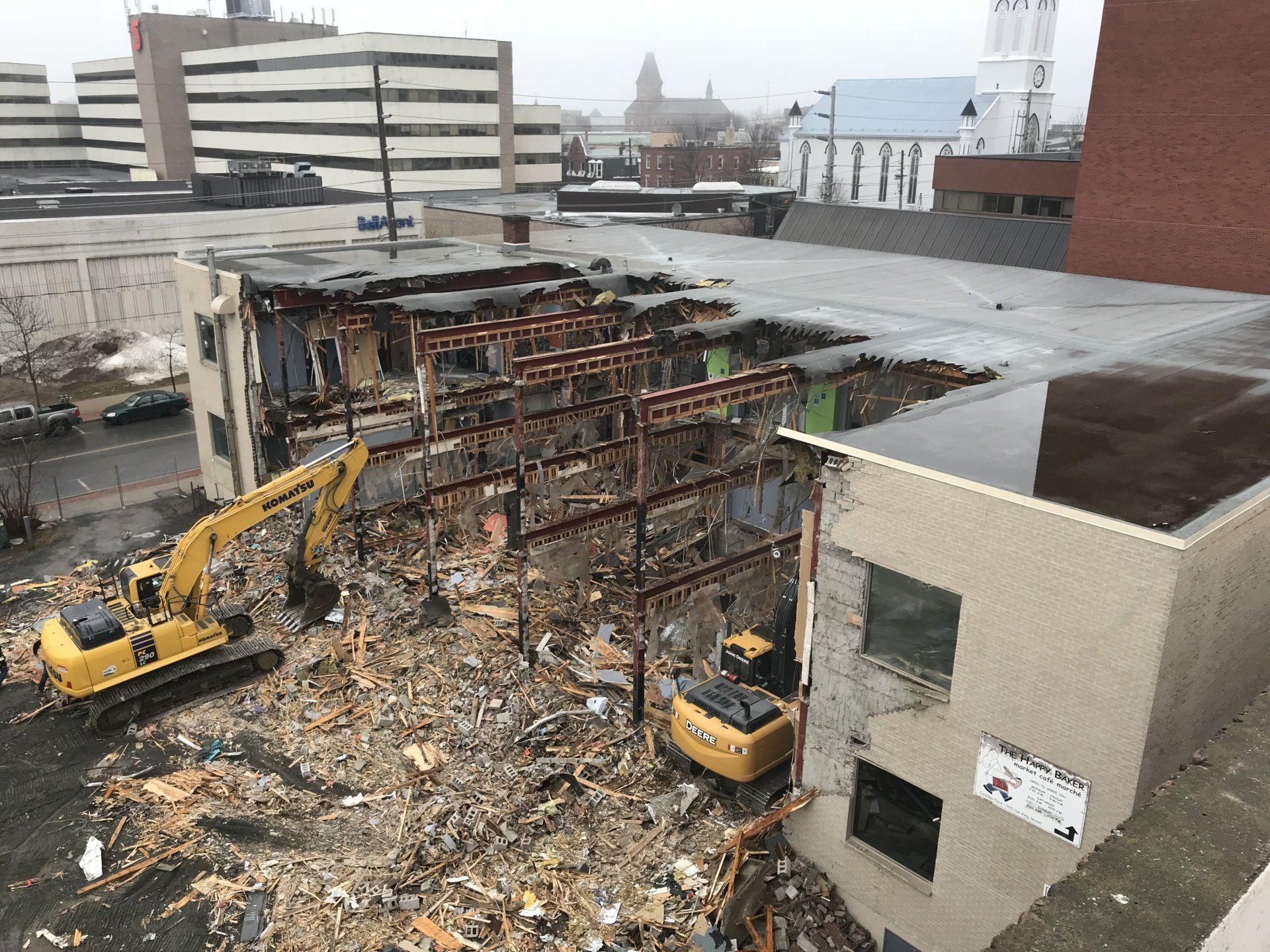A yellow excavator is demolishing a building in a city.
