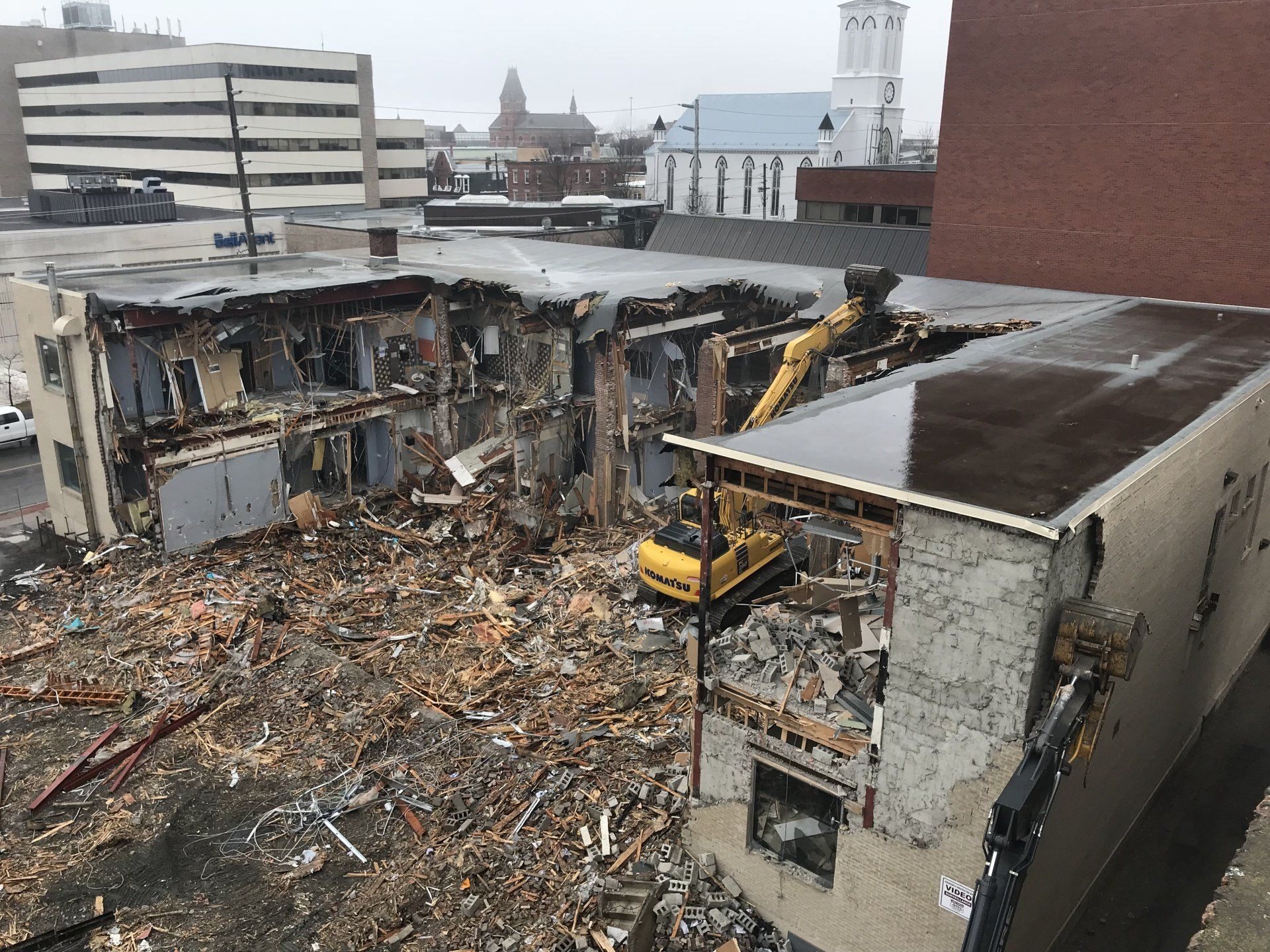 A yellow excavator is demolishing a building in a city.
